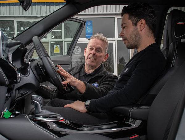 A Unique Mobility engineer talks a male customer through how to use vehicle hand controls in an adapted vehicle