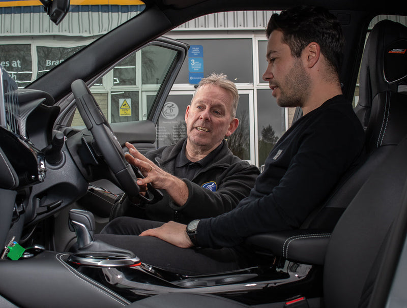A Unique Mobility engineer talks a male customer through how to use vehicle hand controls in an adapted vehicle