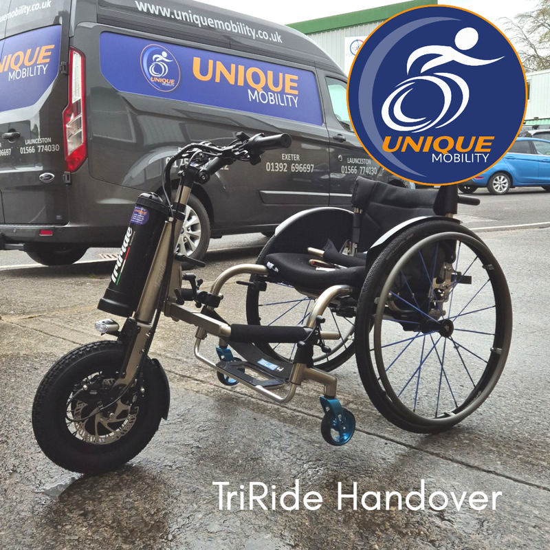 Triride hand bike powered add-on fitted to customers own active wheelchair. In the background is a Unique Mobility branded van 