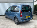 Rear 3/4 view Blue Peugeot Partner WAV parked in front of a corrugated metal wall