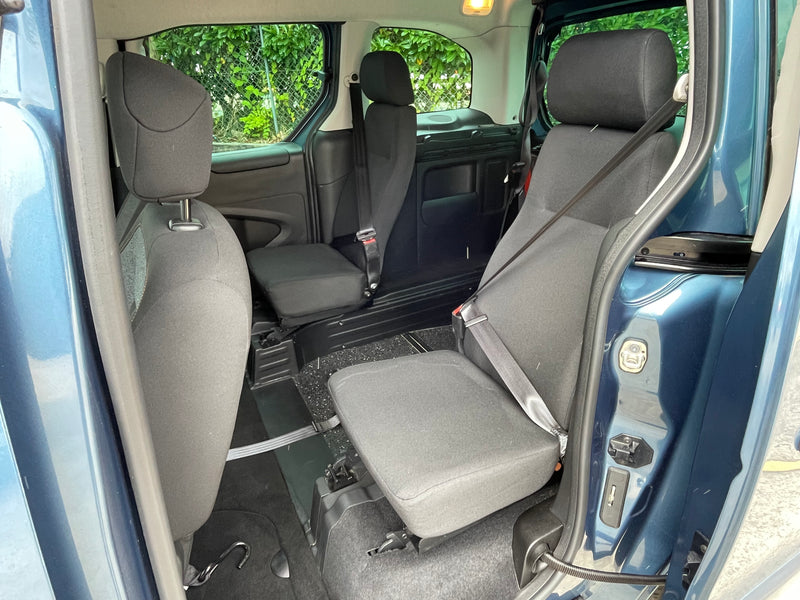 Interior of a wheelchair accessible vehicle with gray seats and open door showing greenery outside
