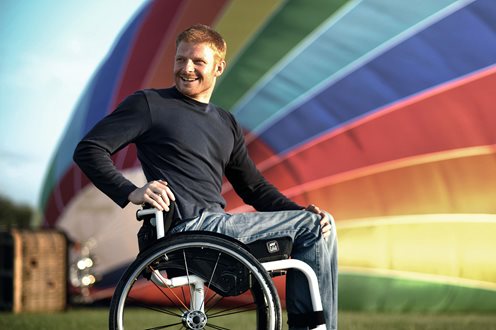 Jay Lite - Wheelchair user in front of colourful hot air balloon being filled in back ground. Jay light cushion shown on white active chair with red-haired male user