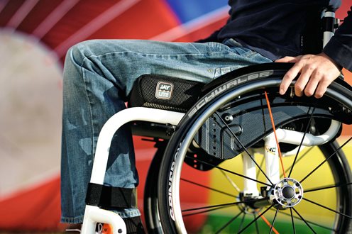 Lay Lite Wheelchair cushion shown on a white framed active chair. Image is cropped to show cushion part of the frame and wheels with the legs and arm of the user. 